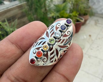 May include: A silver ring featuring an elongated, openwork filigree design shaped like a leaf or wing. A vertical row of seven small, round, multi-colored gemstones in red, orange, yellow, green, light blue, dark blue, and purple is set centrally.
