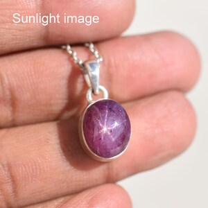 May include: A pendant necklace featuring an oval-shaped, deep magenta star ruby gemstone set in a polished silver bezel. The stone displays a distinct six-rayed star effect on its surface. The text 'Sunlight image' is visible in the upper left corner.