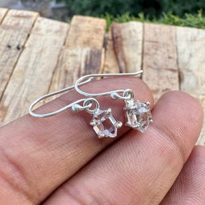 Peut inclure: Boucles d'oreilles pendantes en argent avec des pendentifs en pierres précieuses claires et facettées. Les boucles d'oreilles ont un design simple en forme de crochet et les pierres précieuses sont taillées en forme géométrique.