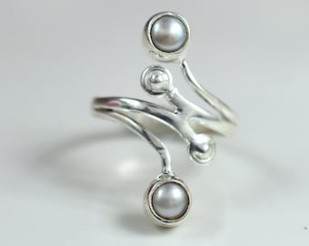 May include: Silver ring with a swirling design and two pearl accents.