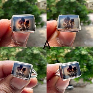 May include: A silver ring with a rectangular agate stone featuring a dendritic pattern in shades of brown and gray. The stone is set in a silver band.