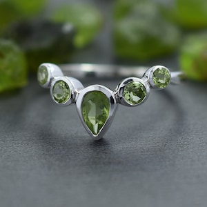 Puede incluir: Un anillo de plata con cinco piedras preciosas verdes en forma de pera engastadas en una banda curva.