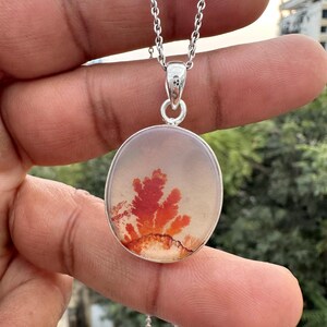 May include: A silver pendant necklace featuring an oval-shaped stone with a natural, fiery red and orange dendritic pattern. The pendant hangs from a delicate silver chain. The stone's design resembles a coral reef or a tree.