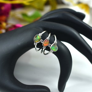 May include: Three silver rings with different colored opal stones. The rings are stacked on top of each other. The opal stones are green, orange, and a light green.