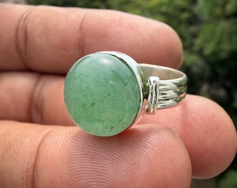 May include: A silver ring featuring a large, round, smooth, light green stone set in a polished metal bezel. The band of the ring is constructed from three parallel silver wires that converge into a single shank at the back of the piece.