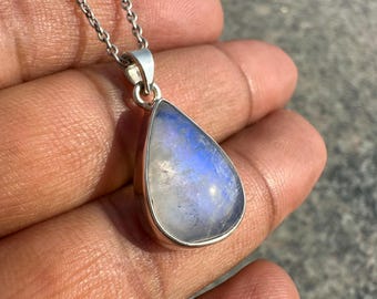 May include: A teardrop-shaped moonstone pendant with a silver setting and chain. The moonstone has a pearlescent, blue and white color. The pendant is displayed against a neutral background.