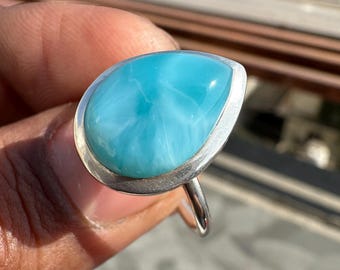 May include: A sterling silver ring featuring a large, teardrop-shaped, light blue gemstone. The stone has a swirling, cloud-like pattern and is set in a polished silver bezel. The ring's band is a simple, rounded design.