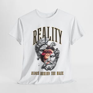 Puede incluir: Camiseta blanca con un diseño gráfico. El diseño incluye la palabra "REALITY" en una fuente audaz y arqueada sobre una imagen dividida de una estatua clásica y un mono con gafas de sol. El texto "HIDES BEHIND THE MASK" está debajo.