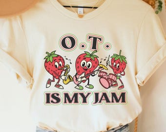 May include: A cream colored t-shirt with a graphic of strawberries playing musical instruments. The text "O.T. is my jam" is printed below the strawberries.