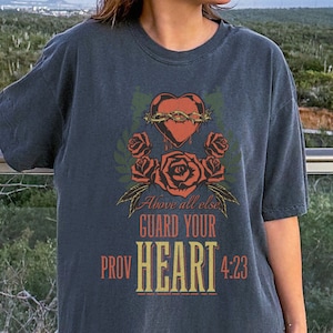 May include: A dark gray oversized t-shirt with a graphic print of a heart with thorns and roses. The text on the shirt reads "Above all else guard your heart Prov 4:23".