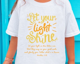 May include: A white t-shirt with a yellow and orange graphic that says "Let your light shine" and a quote from Matthew 5:16. A young girl is wearing the shirt and smiling at the camera.