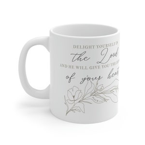 Op de afbeelding: Een witte keramische mok met een zwart bloemenontwerp en de tekst "DELIGHT YOURSELF IN THE LORD AND HE WILL GIVE YOU THE DESIRES OF YOUR HEART PSALM 37:4"