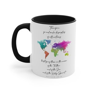 May include: White ceramic mug with a black handle and interior. The mug features a colorful watercolor world map design and script text that reads "Therefore go and make disciples of all nations... Matthew 28:19."