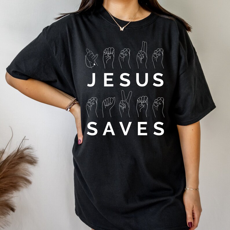 May include: Black t-shirt with the words "JESUS SAVES" in white lettering. The words are spelled out using American Sign Language hand gestures.