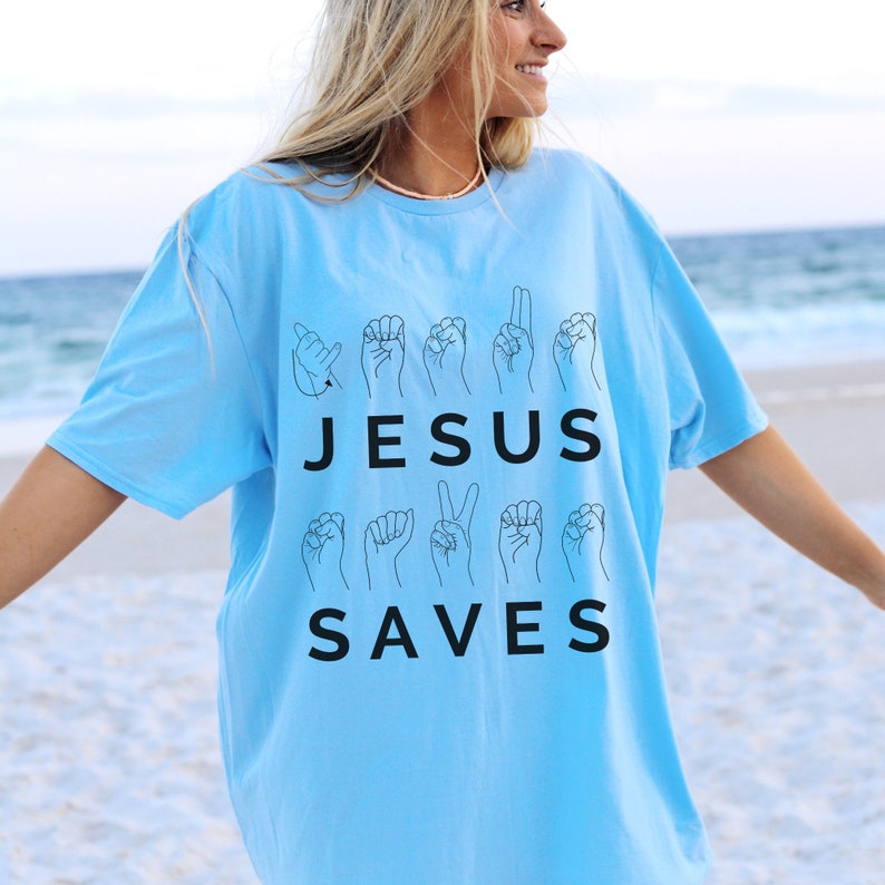 May include: A light blue t-shirt with the words "JESUS SAVES" in black lettering. The words are surrounded by black outlines of hands signing the words in American Sign Language.