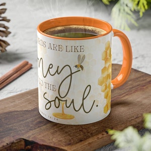 May include: White ceramic mug with an orange rim and handle. The mug features a honeycomb pattern and a bee with the text "Words are like honey to the soul." and the Bible verse "Proverbs 16:24".