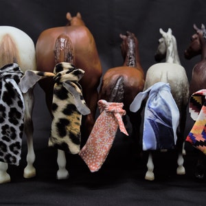 May include: Seven miniature horse figurines with different colored coats and tails. Each horse has a colorful fabric tied around its tail.