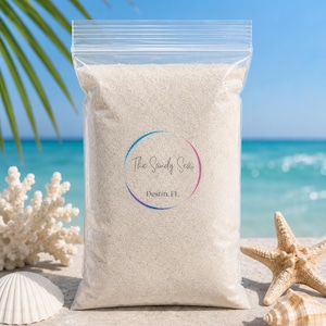 Könnte beinhalten: Ein klarer Plastikbeutel gefüllt mit weißem Sand, mit dem Text "The Sandy Seas Destin, FL" in einem kreisförmigen Design. Der Beutel liegt auf einer sandigen Oberfläche mit einem Seestern, einer Muschel und Korallen im Hintergrund, mit blauem Ozean und Himmel.
