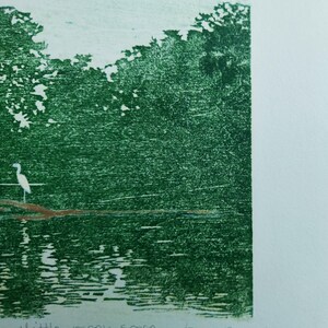 May include: A green-toned print on paper featuring a white bird standing on a brown branch over water, with dense foliage in the background. The text 'little green space' is written in pencil at the bottom left, with a signature on the bottom right.