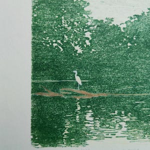 May include: A green-toned print on paper featuring a white heron standing on a brown log in water, with trees in the background. The print is numbered 2/35 and titled 'little green space of calm' in handwritten text at the bottom edge.