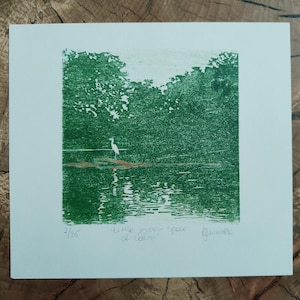 May include: A square print on white paper featuring a green ink landscape of a white heron standing on a log in water. The text "2/35", "little green space of calm", and a signature are written in pencil below the green ink illustration.
