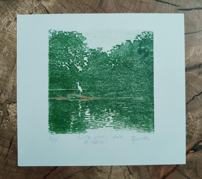 May include: A square print on white paper featuring a green ink landscape of a white heron standing on a log in water. The text "2/35", "little green space of calm", and a signature are written in pencil below the green ink illustration.