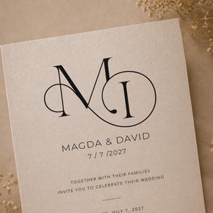 May include: A wedding invitation with a beige background features the initials "MI" in black, intertwined in an elegant design. The names "MAGDA & DAVID" and the date "7/7/2027" are printed below, along with an invitation to celebrate their wedding.