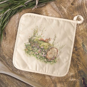 May include: A square, off-white pot holder featuring a watercolor illustration of a squirrel on a moss-covered log with wildflowers. The log has a cut end showing growth rings. A loop is attached for hanging.