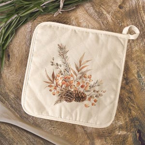 May include: Cream-colored square pot holder with a loop for hanging. The pot holder features a watercolor design of fall foliage, including berries, leaves, and pinecones in shades of brown, orange, and beige. The design is centered on the pot holder.