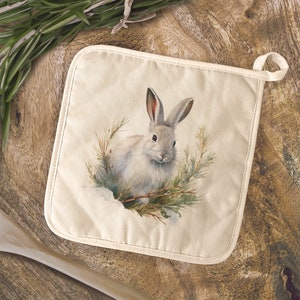 May include: A white cotton pot holder with a brown rabbit illustration surrounded by green pine branches. The rabbit is looking at the viewer with its ears perked up.