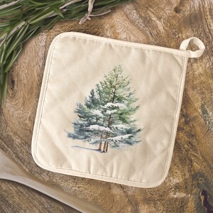 May include: A beige cotton pot holder with a white stitched border features a watercolor illustration of a snow-covered evergreen tree.