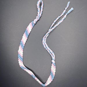 Könnte beinhalten: Ein blaues, rosa und weißes Freundschaftsarmband mit geknüpften Enden.