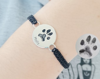 May include: A black cord bracelet with a silver round charm featuring a paw print and the name "Molly" engraved on it.