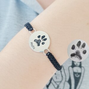 May include: A black cord bracelet with a silver round charm featuring a paw print and the name "Molly" engraved on it.