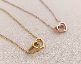 May include: Two gold necklaces with interlocking heart pendants. The pendant on the top necklace is engraved with the name "Aayla" and the pendant on the bottom necklace is engraved with the name "Oscar".
