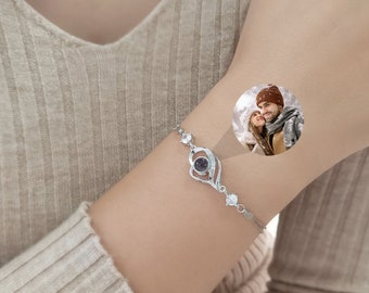 May include: A silver bracelet with a heart-shaped charm that projects a photo of a couple when viewed through a small lens. The bracelet is adorned with small clear crystals.