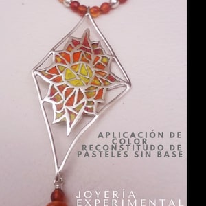 May include: A silver pendant necklace with a geometric design. The pendant features a colorful mosaic of orange, yellow, and red hues. The necklace has a beaded chain and a small, dangling bead cluster. Text on the image reads: "APLICACIÓN DE COLOR RECONSTITUDO DE PASTELES SIN BASE" and "JOYERÍA EXPERIMENTAL".