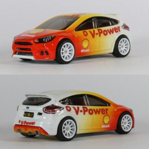 May include: A white and orange toy car with a black spoiler and the words "V-Power" and "Shell" on the side. The car is a Ford Focus.