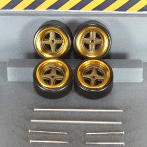 May include: Four black model car wheels with gold rims and a cross-shaped spoke design. Several silver metal rods and pins are also included. The wheels are arranged in a square formation, suggesting a set for a miniature vehicle.