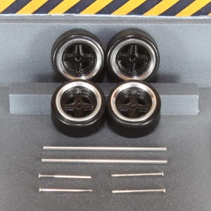 May include: Four black model car wheels with silver rims and a cross-shaped spoke design. Also included are four silver metal rods and two silver metal pins, likely for assembly. The wheels are arranged in a square.