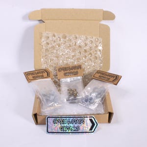 May include: A cardboard box, open to reveal small plastic bags of hardware. Each bag is labelled with "SPECIAL STAGE CUSTOMS" on brown tags. A holographic sticker with the same text is at the bottom. Bubble wrap protects the contents.