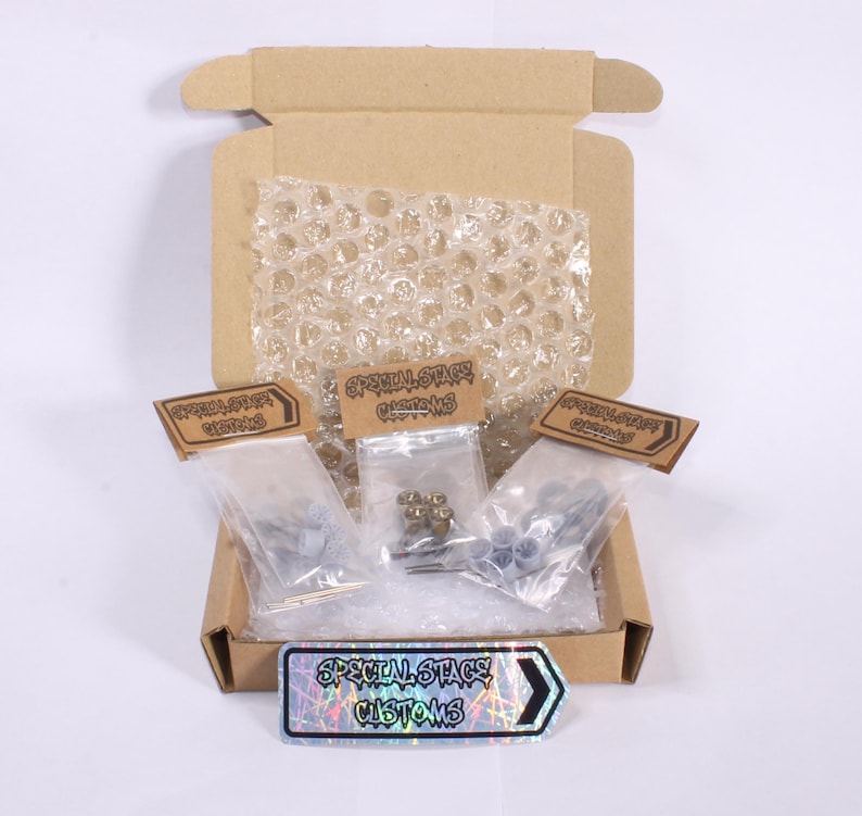 May include: A cardboard box, open to reveal small plastic bags of hardware. Each bag is labelled with "SPECIAL STAGE CUSTOMS" on brown tags. A holographic sticker with the same text is at the bottom. Bubble wrap protects the contents.