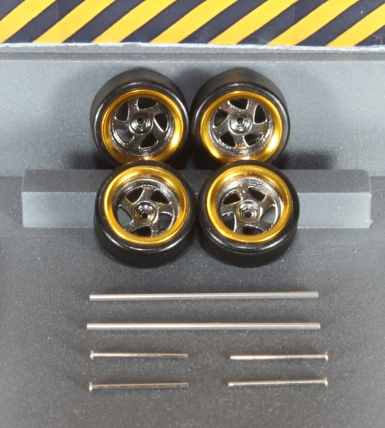 May include: Four model car tyres with gold rims and silver spokes. Several silver metal rods and pins are also included. The tyres are arranged in a square, with the rods and pins below.