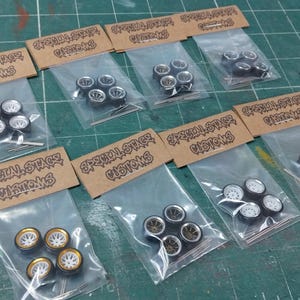 May include: Several sets of model car wheels in clear plastic bags, each with a cardboard header reading "Special Stage Customs". The wheels feature different designs, including silver, gold, and black rims.