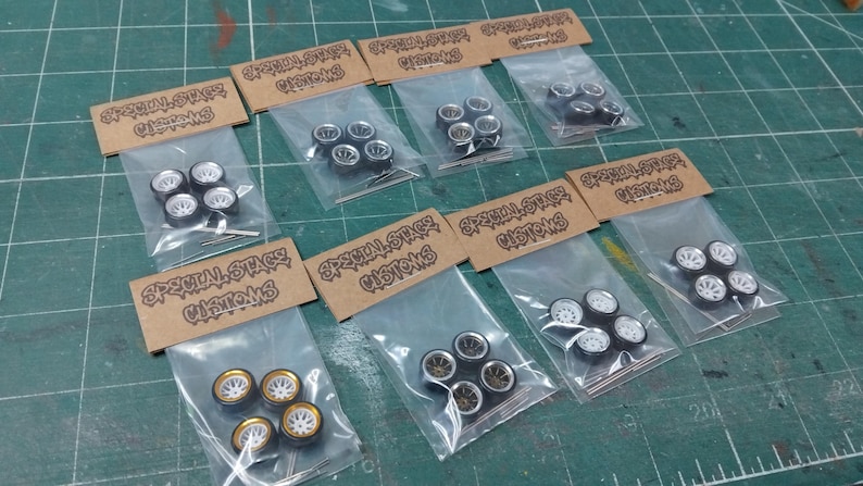 May include: Several sets of model car wheels in clear plastic bags, each with a cardboard header reading "Special Stage Customs". The wheels feature different designs, including silver, gold, and black rims.