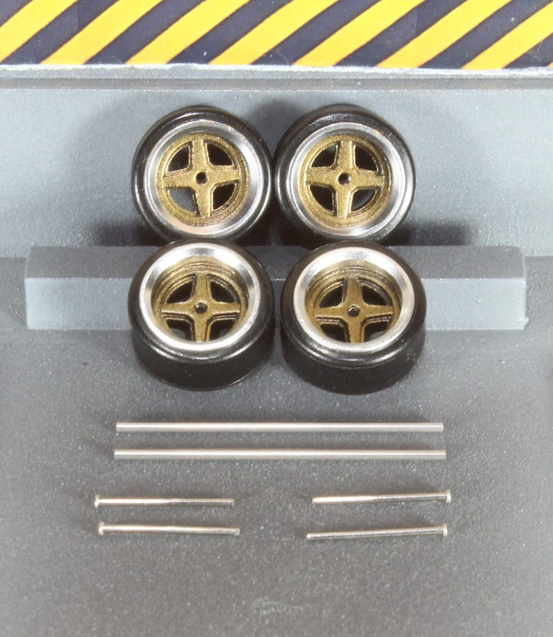 May include: Four black model car wheels with gold-colored centers and silver rims. Also included are six silver metal rods of varying lengths. The wheels are arranged in a square, with the rods below.