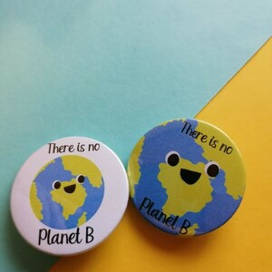 May include: Two round buttons featuring a cartoon image of the Earth. The buttons are white with blue and green accents. The text on the buttons reads "There is no Planet B".