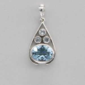 May include: A silver pendant with a teardrop-shaped design featuring a large oval blue topaz gemstone surrounded by four smaller round clear topaz gemstones.