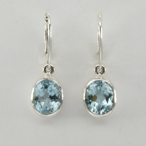 May include: A pair of silver hoop earrings with light blue oval-shaped gemstones hanging from them.