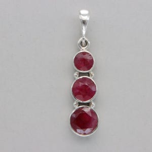 May include: A silver pendant with three round red ruby gemstones.